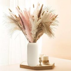 a white vase with some pink and brown feathers in it