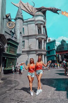 two girls are posing in front of a building with a dragon statue on it's side