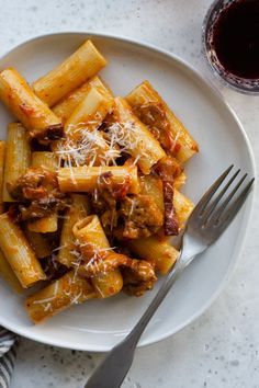 a white plate topped with pasta covered in sauce and parmesan cheese next to a glass of wine