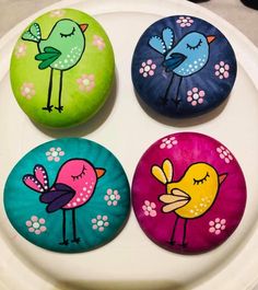 four painted rocks sitting on top of a white plate with flowers and birds on them