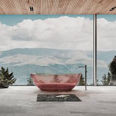 a red bath tub sitting on top of a stone floor next to a large window