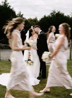 a bride and groom walking with their bridal party in the backgrouds