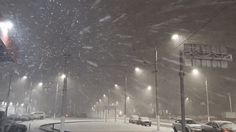 the snow is falling down and cars are parked on the side of the road at night