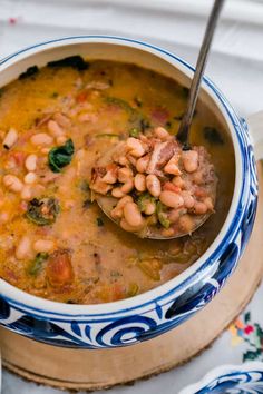 a spoon full of beans and spinach in a blue and white bowl on a table