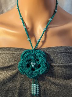 a woman wearing a necklace made with beads and green crocheted fabric on a mannequin head