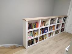 a bookshelf in the corner of a room with wooden floors and white walls