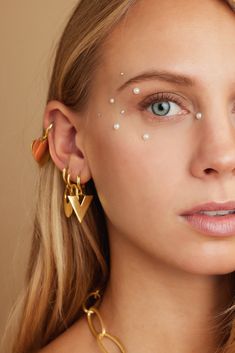 a woman wearing gold earrings with white pearls on her face and ear piercings in the shape of hearts