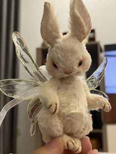 a person holding a stuffed animal bunny with wings on it's back, in front of a computer screen