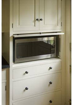 a microwave oven built into the side of a white cabinet with drawers and knobs