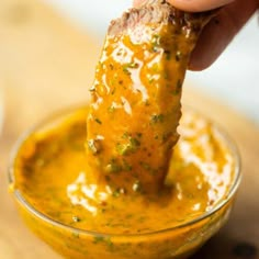 a hand dipping a piece of food into a small glass bowl filled with yellow sauce