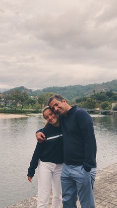 a man and woman standing next to each other near the water on a cloudy day