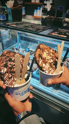 two people holding up ice creams in front of a deli display filled with chocolate and nuts