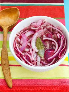 a white bowl filled with red onions next to a wooden spoon on top of a striped table cloth