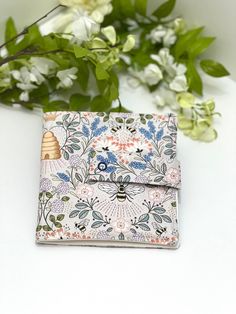 a small wallet sitting on top of a table next to some white flowers and green leaves