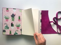 a hand holding an open book with cactus designs on it and pink ribbon around the page