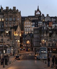 people are walking down the street in front of some old buildings at dusk with lights on