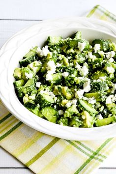 a bowl filled with broccoli and feta cheese on top of a table