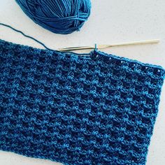 a blue crochet square next to a ball of yarn