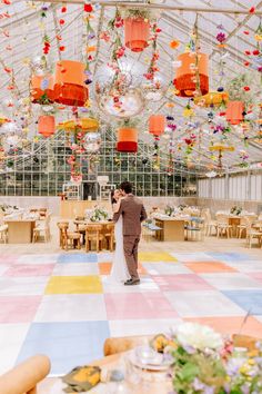 a bride and groom standing in front of an elaborate ceiling decorated with orange, pink, yellow and white paper lanterns