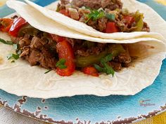 two tacos with meat and peppers on a blue plate