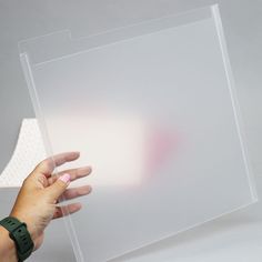 a hand holding a piece of clear acrylic on top of a white surface