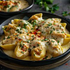 two black plates filled with shells covered in sauce and garnished with parsley