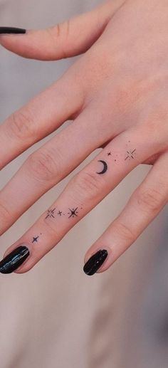 a woman's hand with black nail polish and tattoos on her fingers, which are decorated with stars and the moon