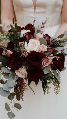 a bridal holding a bouquet of red and pink flowers with greenery on it