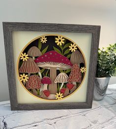 a painting of mushrooms and daisies in a wooden frame on a table next to a potted plant