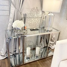 a mirrored console table with candles, flowers and other items on it in front of a curtained window