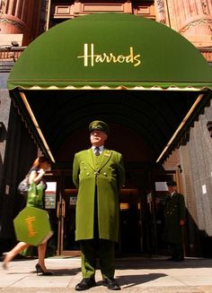 a man in a green suit and hat stands outside the entrance to harrods