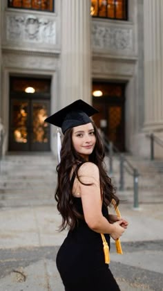 a woman in a graduation cap and gown poses for a photo outside an old building