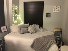 a white bed topped with lots of pillows next to a night stand and lights on the wall