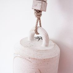 a white ceramic container with a rope hanging from it's top and two hands on the lid