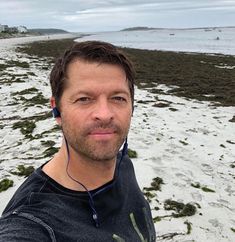 a man standing on top of a sandy beach next to the ocean with headphones in his ears