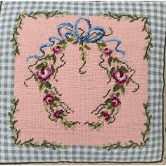 a pink and blue cross stitched pillow with a bow on the front, surrounded by flowers