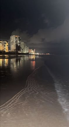 the city lights shine brightly in the dark sky over the water and beach at night