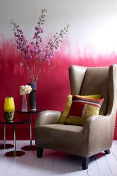 a living room with a chair, table and vase on the floor in front of a red painted wall