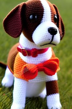 a crocheted dog with a red bow tie sitting in the grass, wearing a sweater