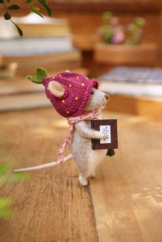 a small mouse wearing a knitted strawberry hat and holding a piece of paper with writing on it