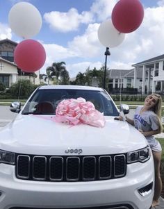 a woman standing next to a white jeep with pink and white balloons on the hood