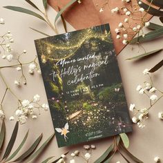 an open book sitting on top of a table next to flowers and greenery in the background