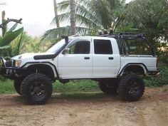 a white truck parked on top of a dirt road next to palm trees and bushes