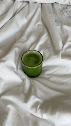 a green drink sitting on top of a white sheet covered bed next to a pillow