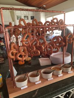 there are many pretzels hanging from the copper rack with dipping sauces on it