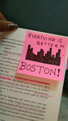 a person holding up a book with a post it note on it that says everything is better in boston