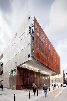 two people walking on the sidewalk in front of a building that is made out of metal