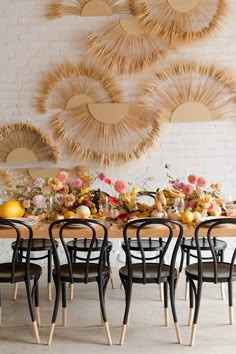 a dining room table with chairs and flowers on the table in front of an artistic wall decoration