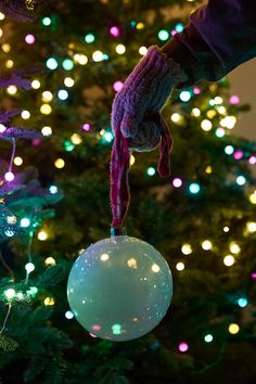 a hand holding an ornament in front of a christmas tree with lights on it