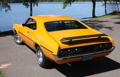 an orange muscle car parked in front of a lake